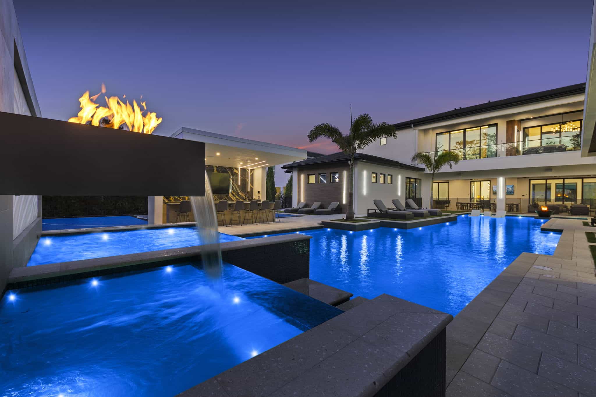 Stunning modern backyard with custom pool, waterfall feature, LED lighting, and ambient fire feature for a luxurious outdoor space in Beacon Lake and Shearwater