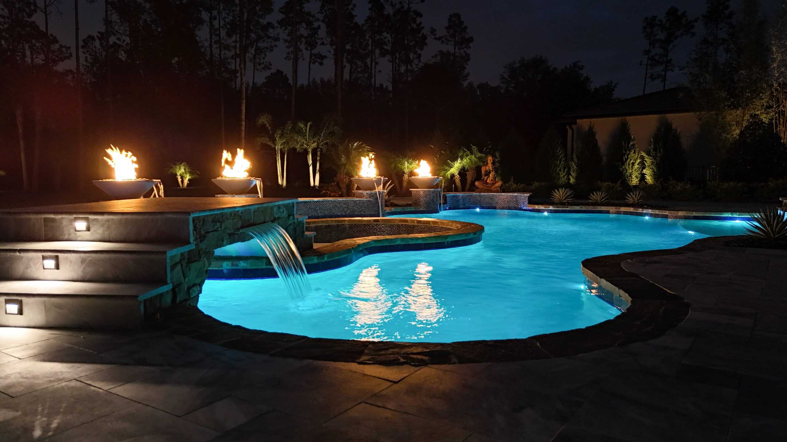 Luxurious illuminated backyard swimming pool at night with fire features and landscaping in West Melbourne