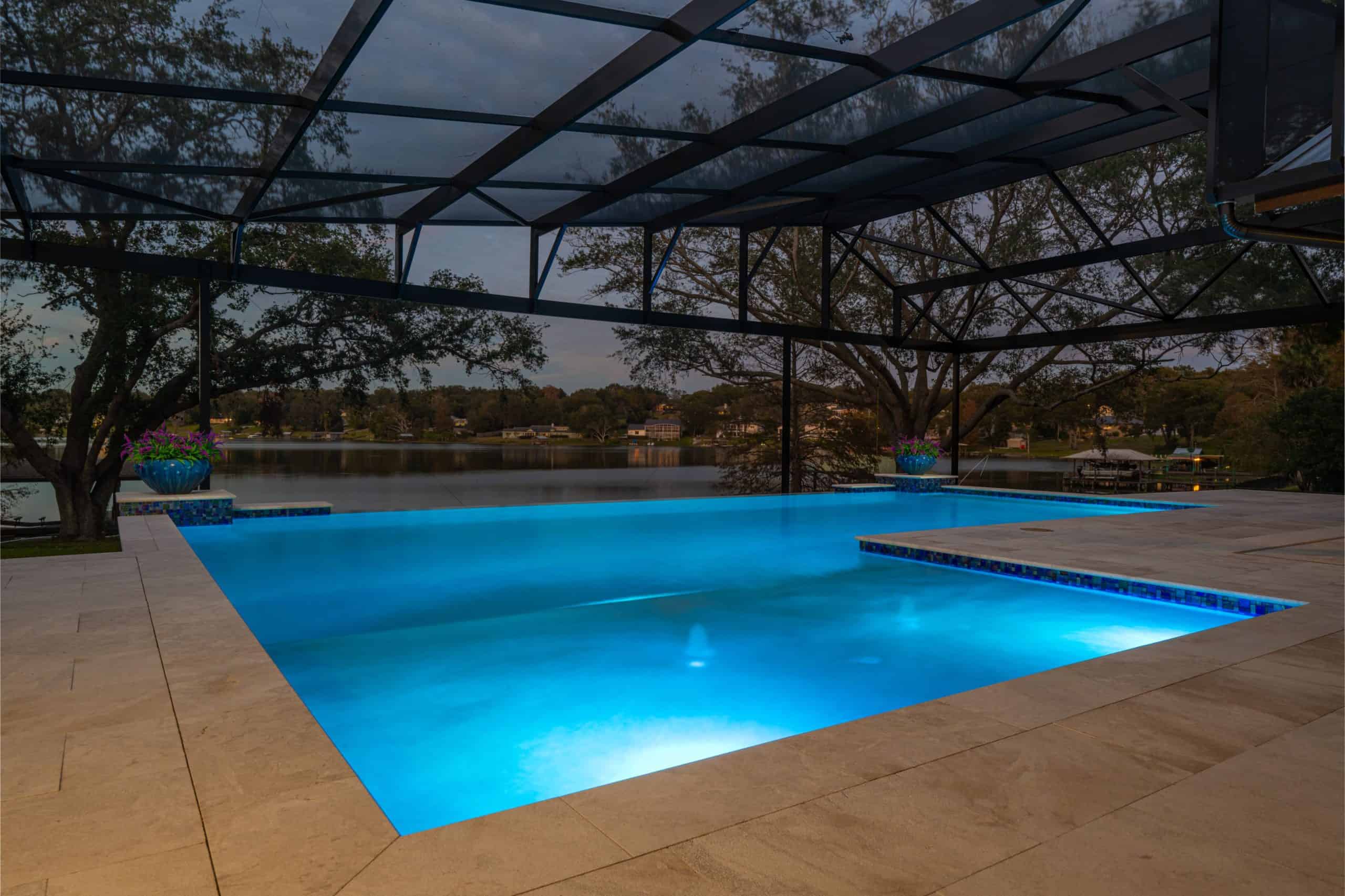 Luxurious illuminated backyard swimming pool under a screened porch with a scenic lake view at dusk in Ponte Vedra Boulevard Oceanfront