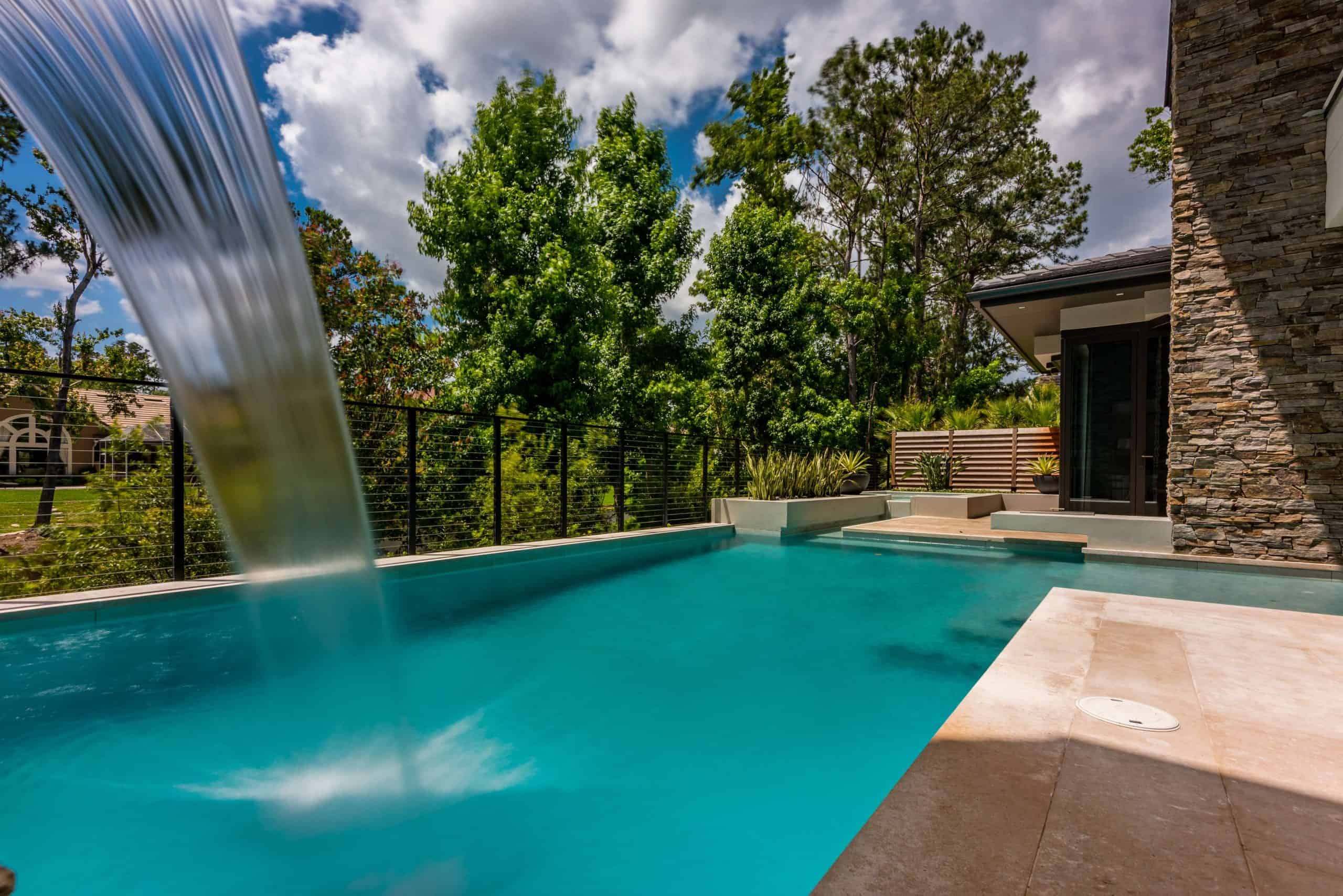 Modern custom pool with waterfall feature and sleek stone accents in a luxurious backyard setting Nocatee St. Johns County FL