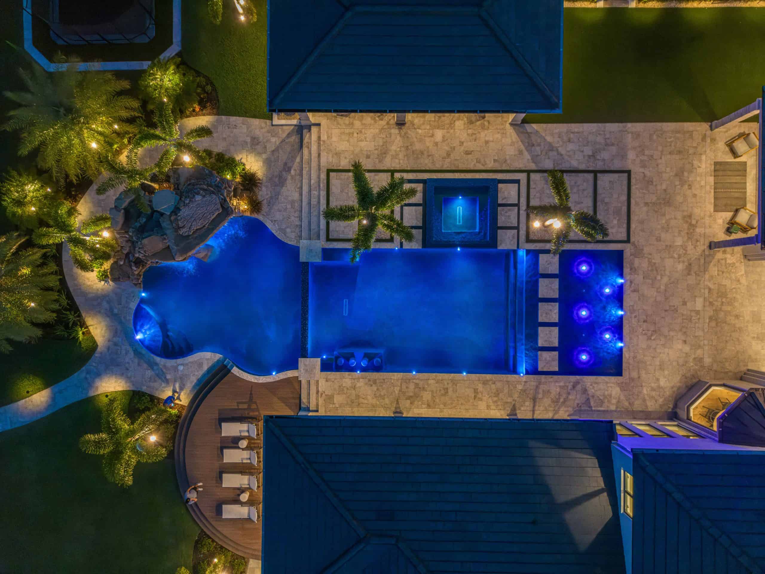 Elegant backyard pool with waterfall, hot tub, and LED lighting surrounded by palm trees and stone patio in St. Cloud, Osceola County FL