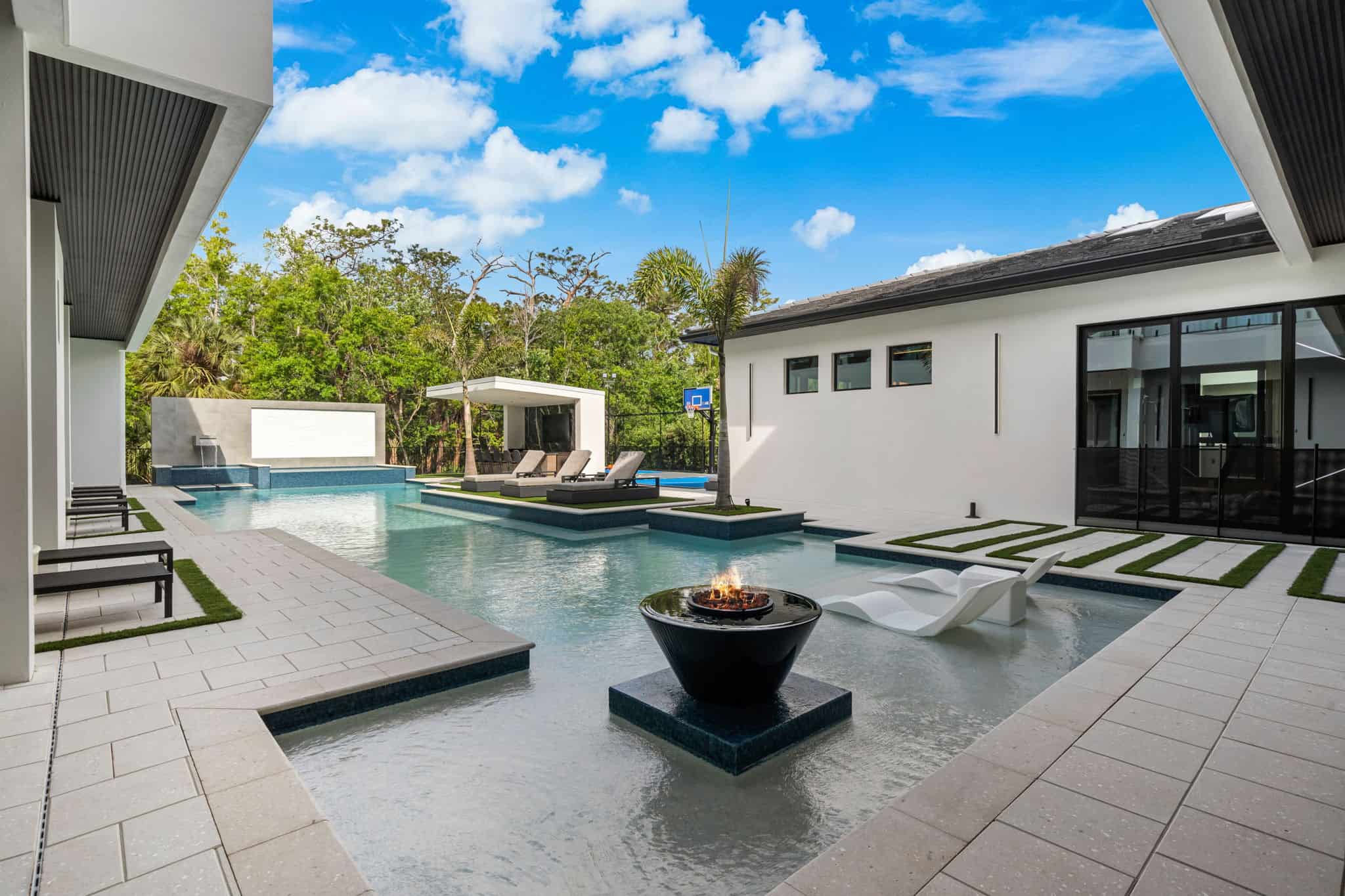 Luxurious modern backyard pool with fire pit, lounge chairs, and lush greenery in Palencia and Madeira