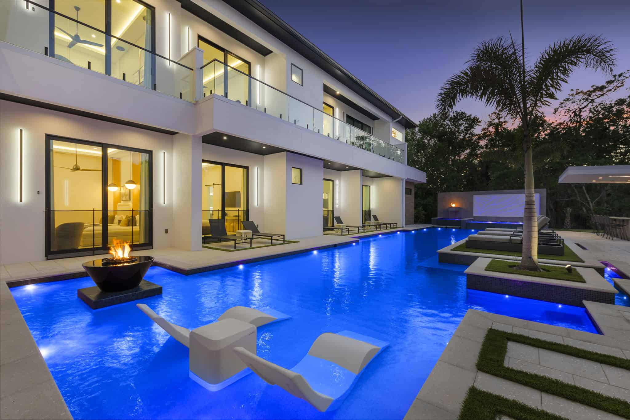 Illuminated backyard pool with outdoor furniture and tropical trees at twilight in Heathrow, Seminole County FL