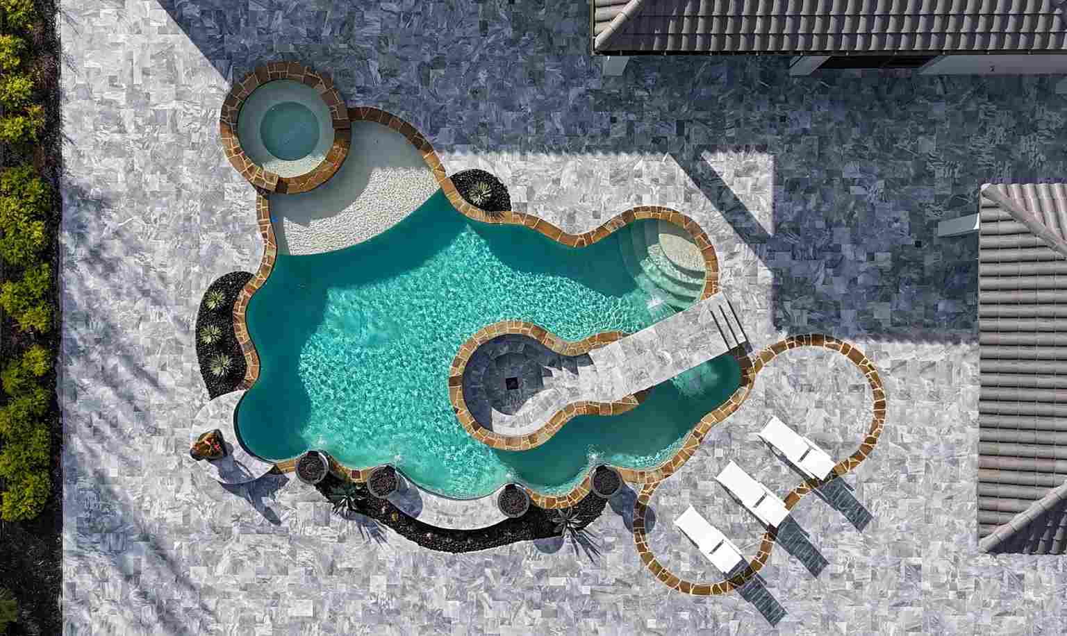 Aerial view of a high-end, custom-shaped swimming pool with spa, cascading waterfalls, and elegant deck in a backyard.