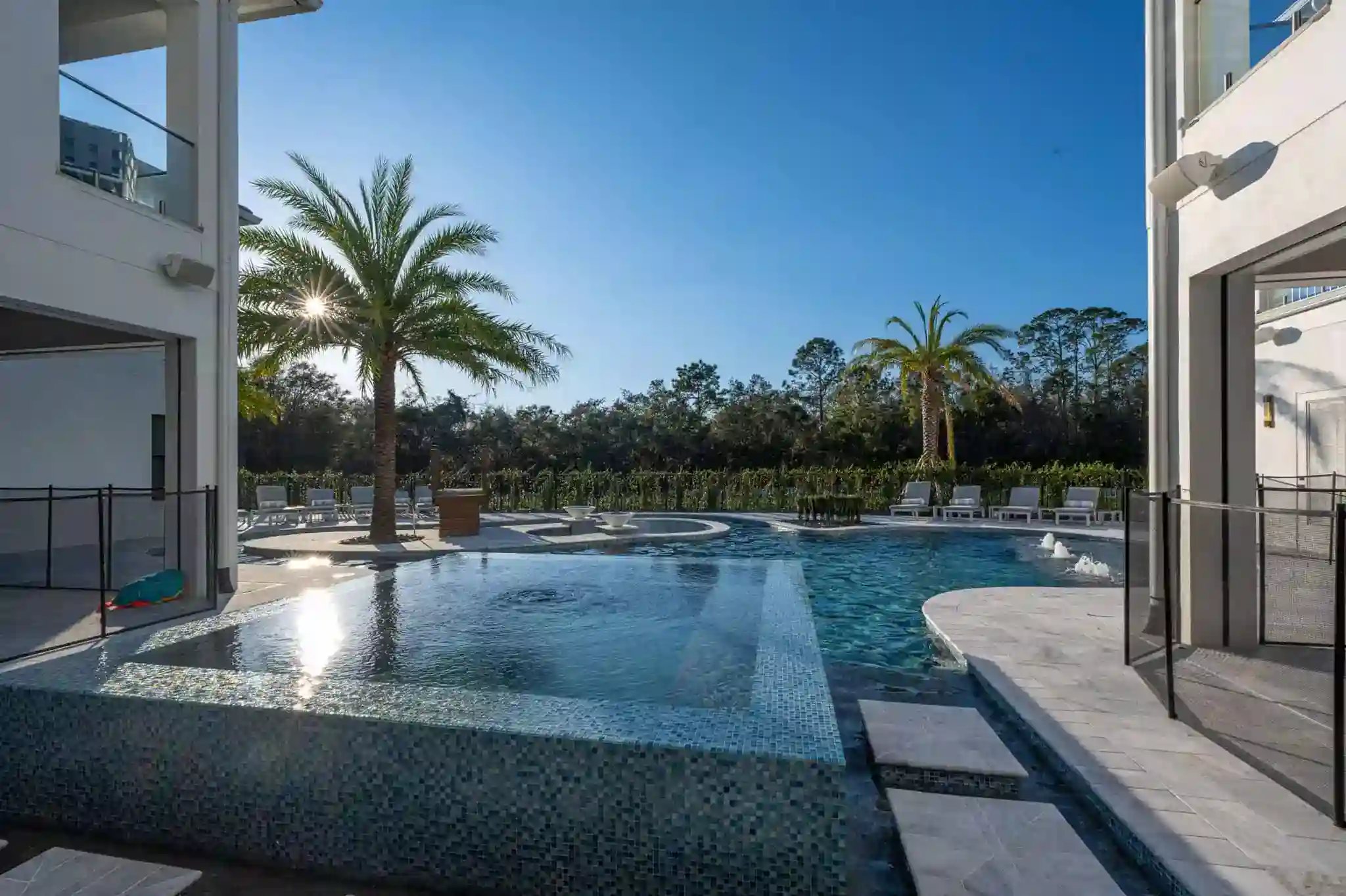 Luxury modern swimming pool with palm tree and outdoor seating area. Aerial view of a custom-designed luxurious pool with lounge chairs, palm trees, and a spa area.