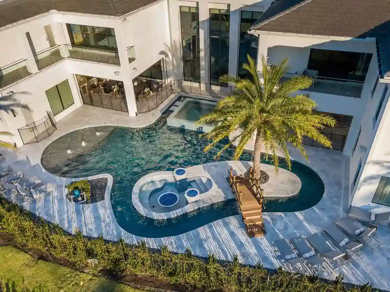 Luxury modern backyard pool with hot tub, lounge area, and palm tree design. Aerial view of a custom high-end pool with hot tub, outdoor lounge, and tropical palm tree in upscale backyard.