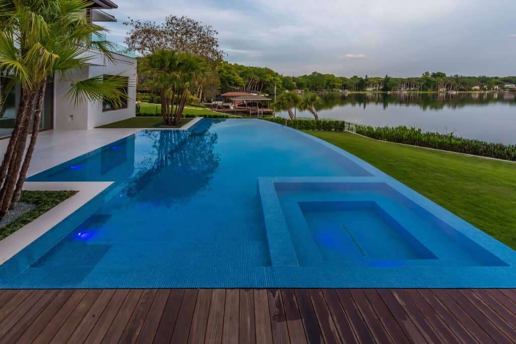 Luxury infinity edge pool and spa overlooking a lake in Sanford, Florida, with a wood deck in the foreground