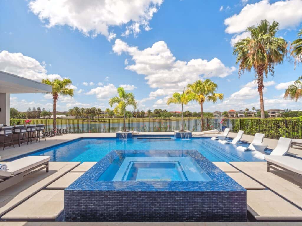 Modern luxury backyard in Central Florida with a rectilinear pool, glass-tile integrated spa and lake view